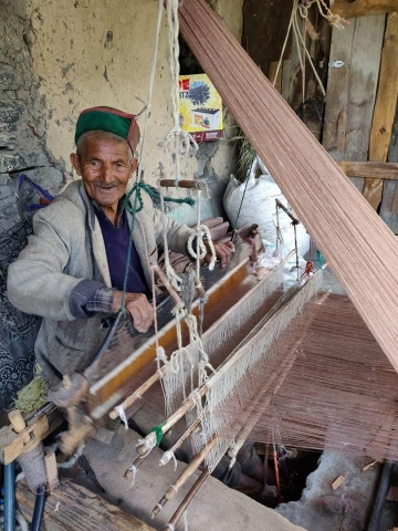 An elderly artist weaving wool on a wooden handloom